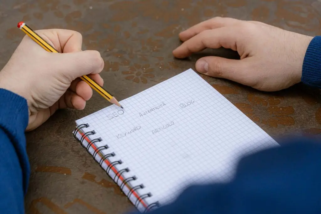 Davide Riccio scrive su un foglio, a matita, delle parole chiave, che sono: seo, autenticità, keyword, blog, articolo